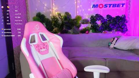 Media: Video of a cozy, well-lit room with a pink gaming chair, gray couch, potted plants, and a \"MOSTBET\" sign, featuring purple and blue lighting.