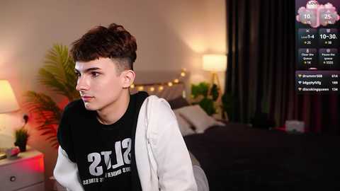 Media: Video of a young man with short, spiky hair and a black and white hoodie, standing in a dimly lit bedroom with a bed, potted plants, and a digital clock displaying 6:09 PM.