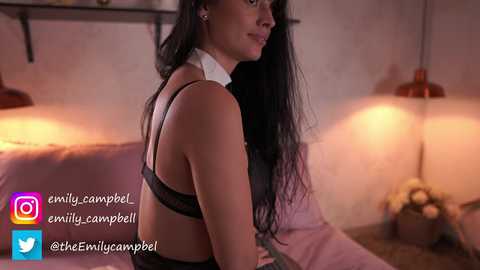 Media: Video of a woman with long black hair, wearing black lingerie, in a dimly lit room with a pink couch and two red lamps.