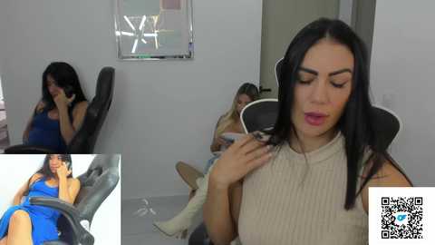 Media: Video of a woman with long black hair, wearing a beige ribbed sweater, sitting in a chair, adjusting her headphones in a minimalist room.