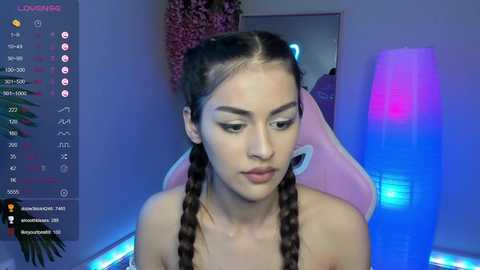 Media: A video of a young woman with long, braided hair, wearing minimal makeup, sitting in a pink gaming chair with a blue light background.