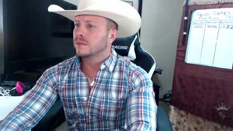 Media: Video of a white man with a short beard, wearing a white cowboy hat and plaid shirt, seated at a desk in an office.