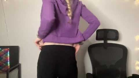 Media: A video of a blonde woman with a light skin tone, wearing a purple jacket and black pants, standing in a room with a black chair and colorful abstract painting.