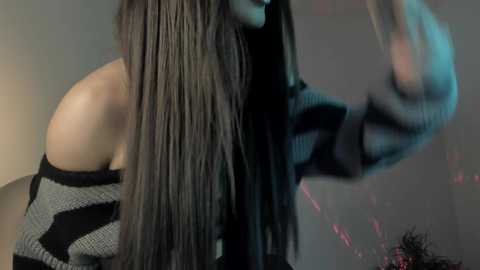 Media: A video of a woman with long, straight, dark hair, wearing a black, off-the-shoulder, striped sweater, captured in a blurred, motion-filled indoor setting with soft lighting.