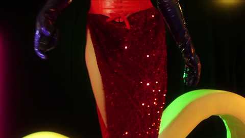 Media: Video of a person wearing a shiny, red sequined dress with a slit, black gloves, and a green and yellow inflatable ring, set against a dark background.