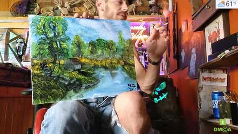 Media: A man with a beard, wearing a black t-shirt, paints a colorful landscape on canvas, surrounded by books, posters, and a red chair in a cozy, cluttered room.