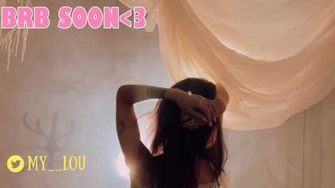 Media: A video of a woman with long, dark hair, wearing a white dress, stands with her arms raised, silhouetted against a soft, beige, draped background. The image features the text \"BRR SOOK\" in bold, pink letters.