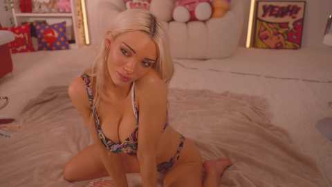 Media: Video of a blonde, fair-skinned woman in floral bikini, kneeling on a beige bed in a colorful, cartoon-themed bedroom with stuffed animals and posters.