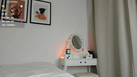 Media: A video of a minimalist, modern bedroom with white walls, a white vanity table, a large oval mirror, a white bed, beige curtains, and two abstract art pieces on the wall.