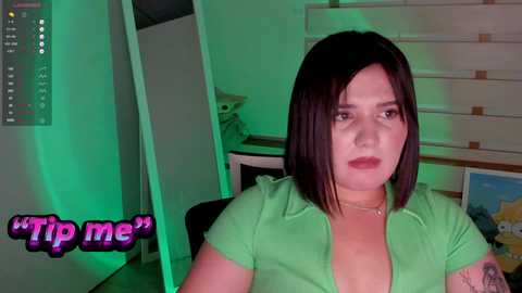 Media: Video of a young, light-skinned woman with shoulder-length dark hair, wearing a green top, sitting in a dimly lit room with green lighting, captioned \"MyM\" in pink.