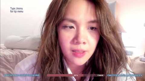 Media: A video of an Asian woman with long, wavy brown hair, light skin, and a neutral expression, wearing a white shirt. The background shows a bed with gray sheets and a lamp. Text overlays indicate \"Type: Anime for menu\" and \"OnlyFans.com/ikimiss.\