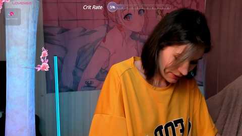 Media: Video of a young woman with shoulder-length black hair, wearing a yellow T-shirt, standing in a room with a pink poster and blue neon lights.