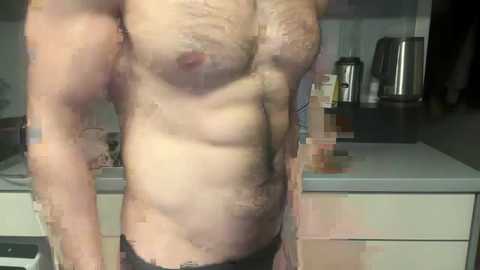 Media: Video of a muscular, shirtless man in black underwear standing in a kitchen with a countertop, stainless steel kettle, and dark cabinets in the background.