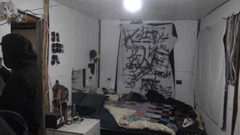 Media: A video of a messy, graffiti-covered bedroom with a person in black hoodie and jeans, a chaotic bed with colorful blankets, and a cluttered white wall with tags.