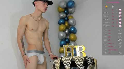 Media: Video of a shirtless, lean, white man in white briefs, holding a cake with \"THB\" letters, in a room with balloons and a birthday-themed display.