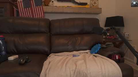 Media: A video of a cluttered living room with a brown leather sofa, an American flag, a black lamp, a red glass, and a beige blanket.