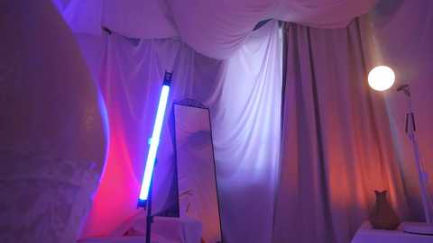 Media: Video of a cozy, dimly lit bedroom with a large, framed mirror, white sheer curtains, a glowing red light, and a soft, spherical light emitting a warm glow.