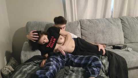 Media: Video of a young man with short brown hair, shirtless, hugging another man with long brown hair on a gray couch, both in pajamas.