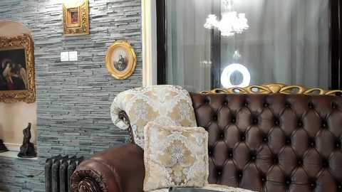 Media: Video of a luxurious living room featuring a brown leather tufted sofa with floral cushions, a textured grey stone wall, framed art, and a modern chandelier.