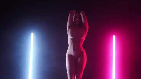 Media: Video of a nude, slender woman with small breasts and pale skin, arms raised, standing between two bright pink and blue neon lights against a dark, foggy background.