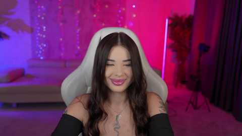 Media: Video of a smiling woman with long dark hair and a white veil, wearing black gloves, in a dimly lit room with purple and pink lights.