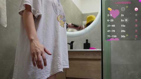 Media: Video of a person in a white t-shirt standing in a bathroom, mirror reflection showing another person with a yellow hat brushing teeth.