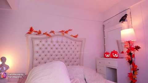 Media: Video of a cozy, white-themed bedroom with a tufted headboard, Halloween decorations, including carved pumpkins and orange leaves, and a white vanity with a mirror and lamp.