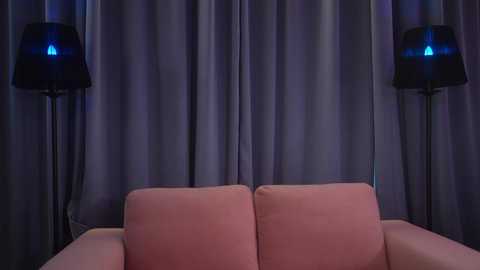 Media: Video of a modern living room with a pink sofa against a backdrop of gray curtains, featuring two black floor lamps with blue LED lights.