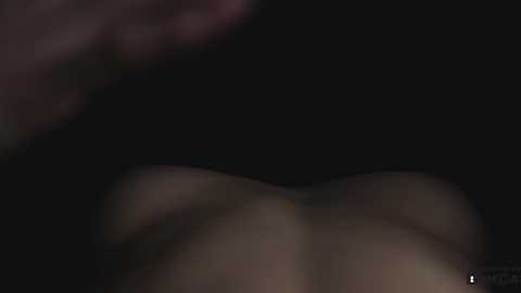 Media: A dimly lit, close-up video of a nude, light-skinned person with visible breasts and a hint of pubic hair, taken from a low angle, focusing on the chest area.