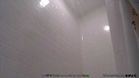 Media: Video of a white-tiled shower with steam, featuring a blurred figure in the background, likely a person showering. The tiles are smooth and reflective. Water droplets and condensation are visible.