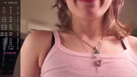 Media: Video of a fair-skinned woman with light brown hair, wearing a pink spaghetti-strap tank top and a silver necklace. Background shows a calendar with \"Love Letter\" written in red.