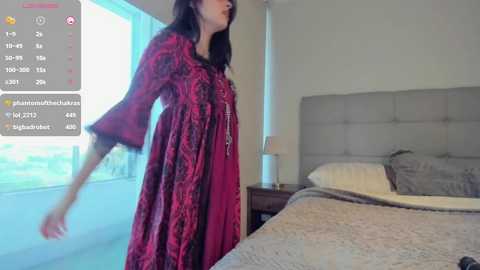 Media: A video of a woman in a red, floral-patterned dress dancing in a modern bedroom with a gray upholstered headboard and white bedding.