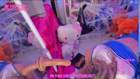 Media: Video of a woman wearing a blue and white outfit, lying on a bed with a large, pink teddy bear, surrounded by plush toys and a realistic dildo.