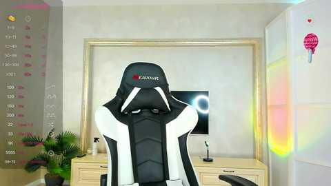 Media: Video of a black and white gaming chair with \"FANTIK\" branding, in a modern, minimalist room with a flat-screen TV, a potted plant, and decorative wall art.