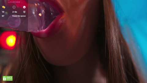 Media: A close-up video of a woman's open mouth, with a clear, glowing object inside, set against a blurred blue and red background.