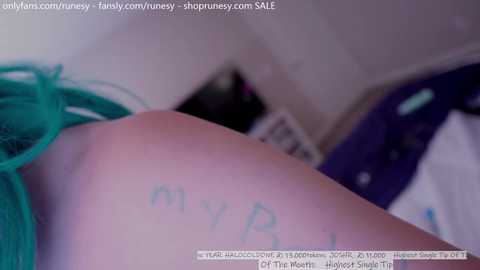 Media: Video of a person's arm with green feathers and \"my PR\" written in blue marker, blurred background.