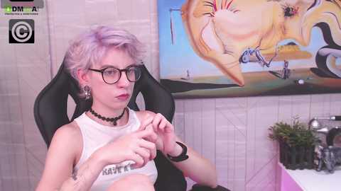 Media: Video of a pale, short-haired, androgynous person with glasses, wearing a white tank top and black choker, fidgeting with their hands. Background features a colorful abstract painting and a pink sink.