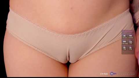 Media: A video of a woman's lower torso in beige panties, showing a slight waist and a smooth, fair skin tone. The background is black, emphasizing the fabric texture and body contours.