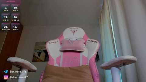 Media: A video of a pink and white gaming chair with a beige cushion, positioned in a room with a wooden door and white curtain.