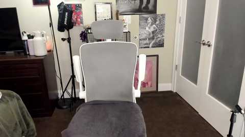 Media: Video of a home office with a white chair, beige walls, black floor lamp, and various framed art.