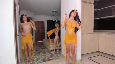 Media: Video of a young, slender, topless woman with long black hair in a yellow dress, posing in a modern, minimalist living room with beige furniture.