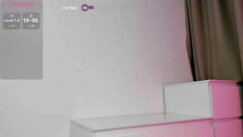 Media: Video of a minimalist room with a white wall and a purple, textured chair. A digital clock displaying \"10:50\" is mounted on the wall. A curtain partially covers the right side.