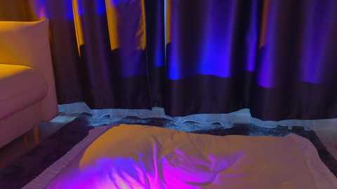 Media: Video of a dimly lit room with a yellow couch, dark curtains illuminated by purple and blue lights, and a fluffy white pillow on a plush rug.