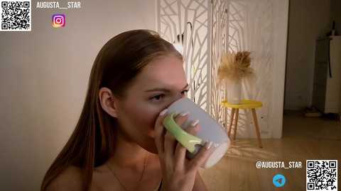 Media: Video of a young Caucasian woman with light skin and straight, long brown hair, drinking from a green and white sippy cup. She has a neutral expression. Background features a modern, minimalist room with beige walls and a small yellow stool. QR codes and social media handles are visible.