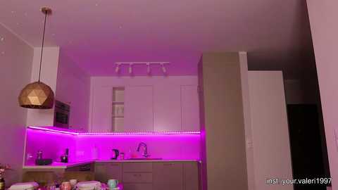 Media: Video of a modern, minimalist kitchen with white cabinets, purple LED strip lighting, and a wooden pendant light.