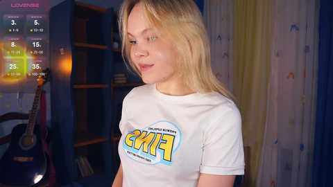 Media: A video of a blonde woman with shoulder-length hair wearing a white t-shirt with \"CHiP\" text, standing in a room with bookshelves and a guitar.