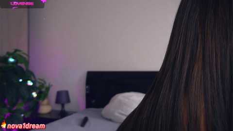 Media: A video shows a woman's long, straight black hair cascading over a white pillow on a bed, with a black lamp and green plants in the background. The room has a modern, minimalist vibe.