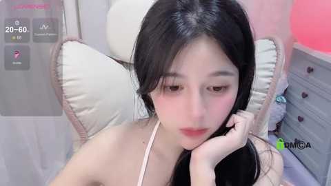 Media: A video of an East Asian woman with long black hair, light skin, and pink lipstick, resting her head on a white pillow, wearing a white strapless top.