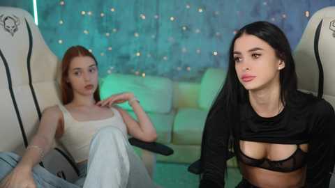 Media: Video of two young women in a dimly lit room. One wears a white crop top, revealing her breasts, and the other a black top, exposing cleavage.