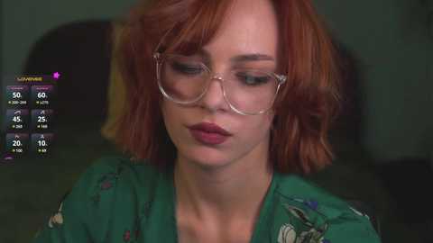 Media: A video of a woman with red hair and glasses, wearing a green floral blouse, set against a dark background.